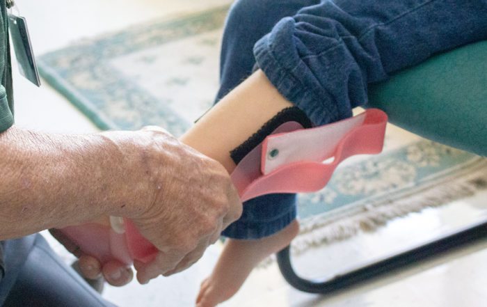 close up of a man's hand's putting a leg brace on a child's leg.